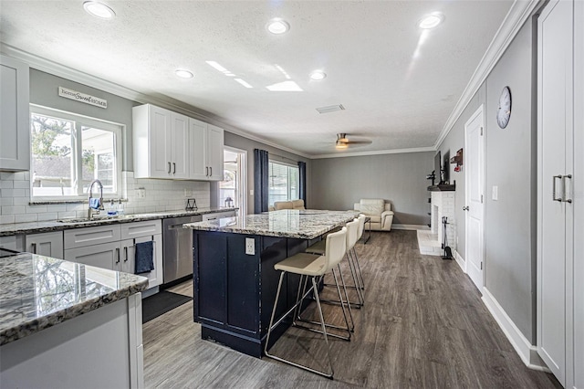 kitchen featuring light stone counters, a center island, ornamental molding, dishwasher, and white cabinets