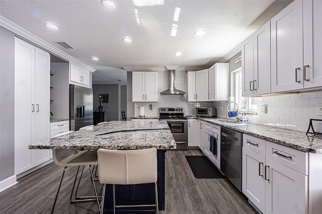 kitchen featuring a breakfast bar area, appliances with stainless steel finishes, light stone counters, a kitchen island, and wall chimney exhaust hood