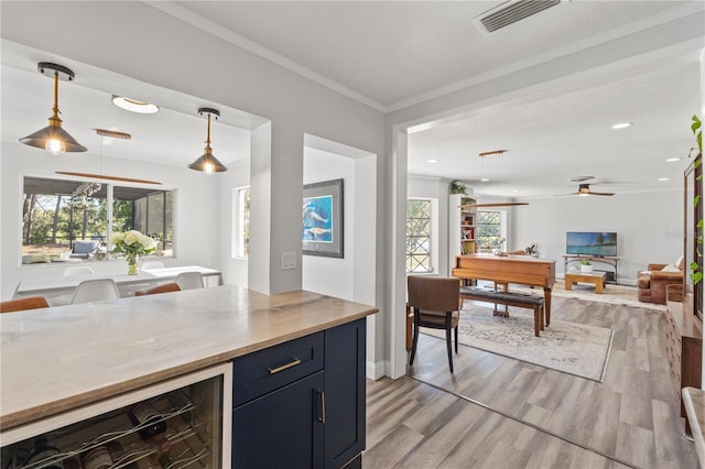 kitchen with pendant lighting, crown molding, ceiling fan, beverage cooler, and light wood-type flooring