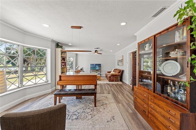 dining space featuring ceiling fan, crown molding, light hardwood / wood-style floors, and a textured ceiling