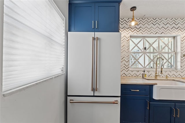 kitchen with sink, high end fridge, tasteful backsplash, blue cabinets, and decorative light fixtures