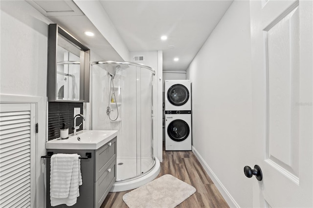 bathroom with walk in shower, stacked washer / drying machine, tasteful backsplash, vanity, and hardwood / wood-style floors