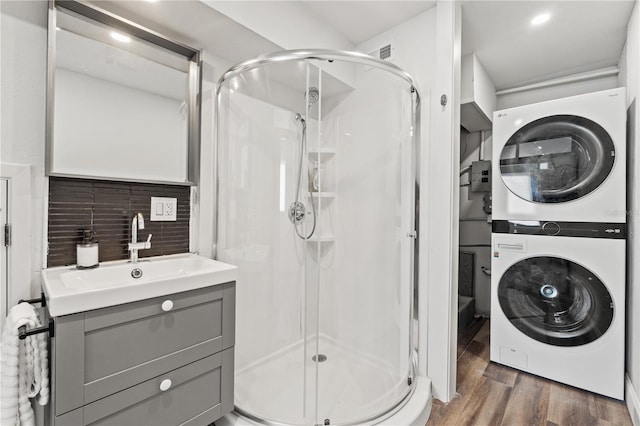 bathroom with hardwood / wood-style floors, backsplash, stacked washer and dryer, vanity, and a shower with door