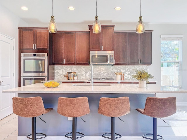 kitchen featuring sink, light tile patterned floors, stainless steel appliances, and an island with sink