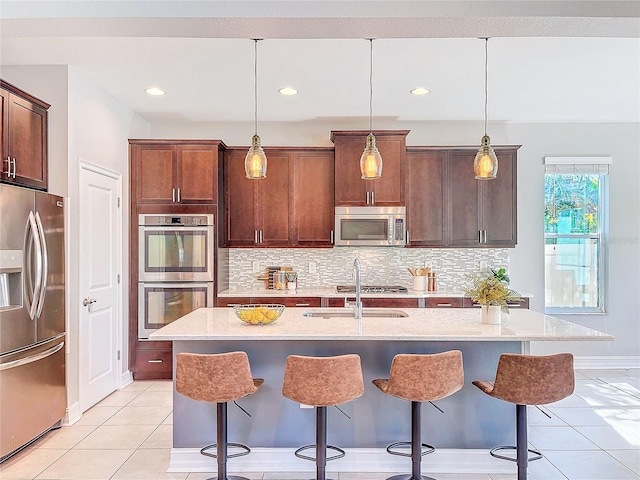 kitchen with pendant lighting, an island with sink, sink, light tile patterned floors, and stainless steel appliances