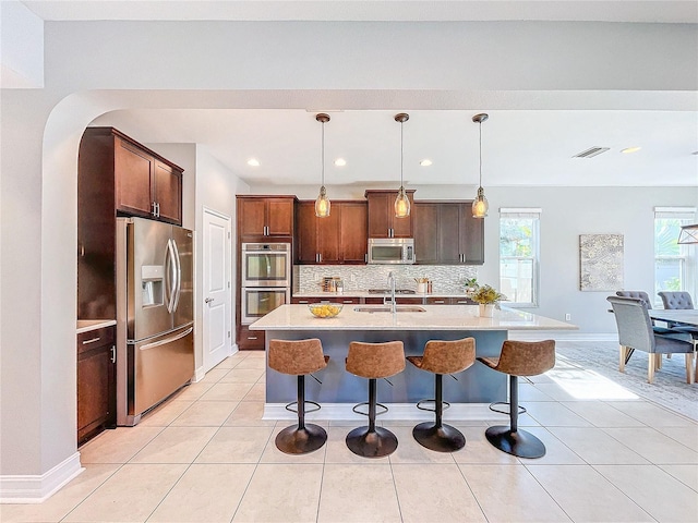 kitchen featuring sink, backsplash, hanging light fixtures, stainless steel appliances, and a center island with sink