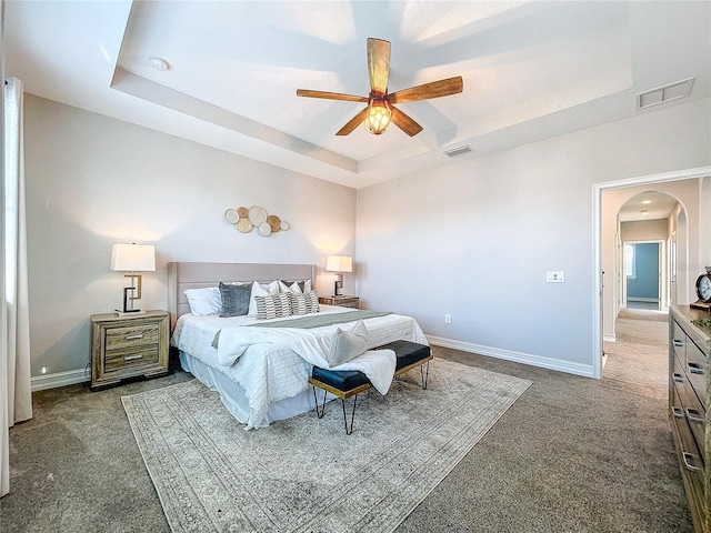 carpeted bedroom with ceiling fan and a raised ceiling