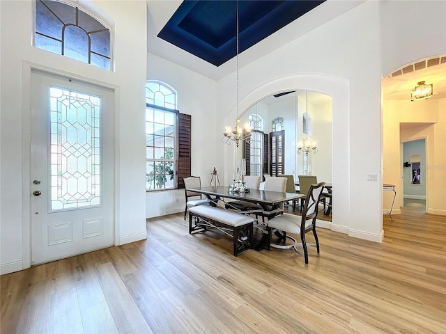 dining area featuring light wood-type flooring, a high ceiling, and a notable chandelier