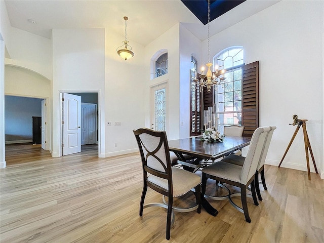 dining space with a notable chandelier, a towering ceiling, and light wood-type flooring