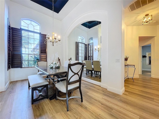 dining space with an inviting chandelier, a towering ceiling, and light hardwood / wood-style flooring