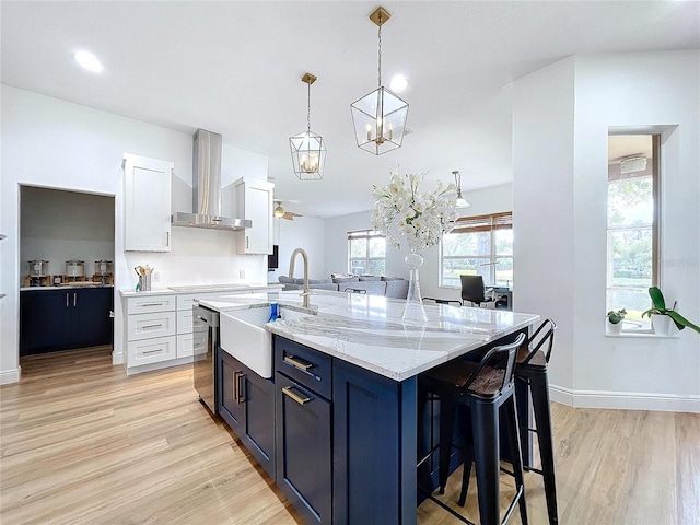 kitchen featuring pendant lighting, sink, white cabinets, a center island with sink, and wall chimney exhaust hood