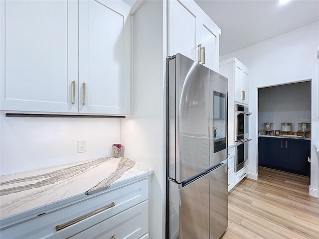 kitchen with white cabinetry, light stone countertops, light hardwood / wood-style floors, and appliances with stainless steel finishes