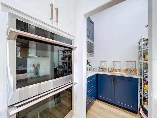 kitchen featuring blue cabinetry, stainless steel double oven, and light hardwood / wood-style flooring