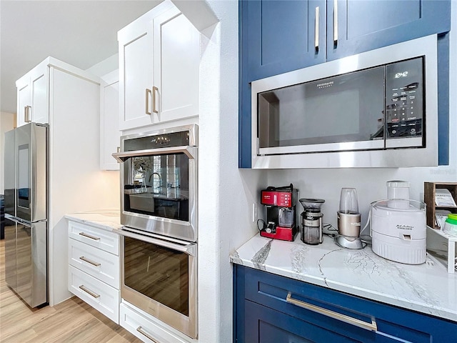 kitchen featuring stainless steel appliances, blue cabinets, white cabinets, and light stone counters