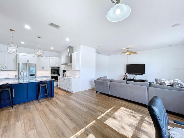 kitchen with decorative light fixtures, white cabinets, a kitchen breakfast bar, and wall chimney exhaust hood