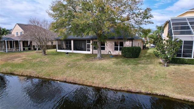 rear view of house with a water view, a lawn, and a sunroom