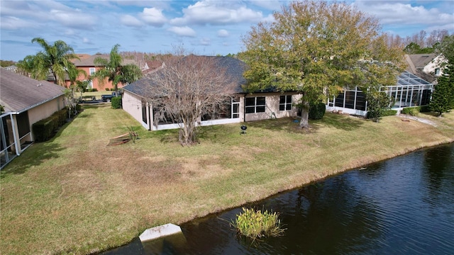 rear view of house featuring a lanai, a water view, and a lawn