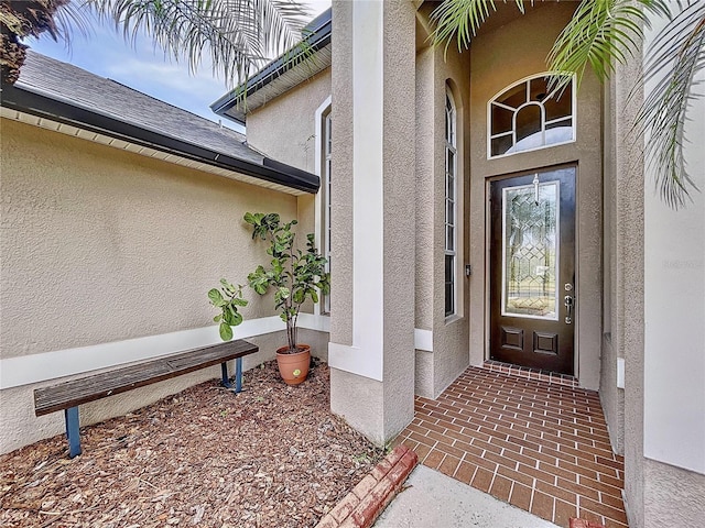 entrance to property featuring roof with shingles and stucco siding