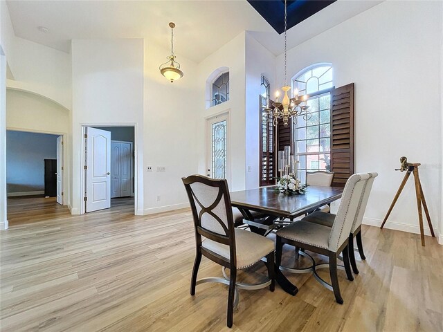 dining area featuring baseboards, a high ceiling, light wood-type flooring, and a notable chandelier