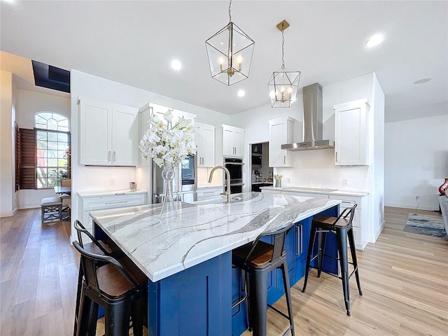 kitchen featuring white cabinets, a spacious island, a breakfast bar area, wall chimney range hood, and pendant lighting