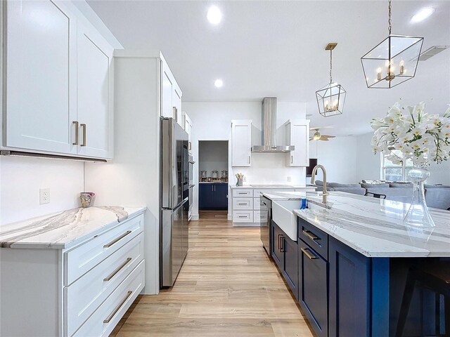 kitchen with a sink, white cabinets, hanging light fixtures, light stone countertops, and wall chimney exhaust hood