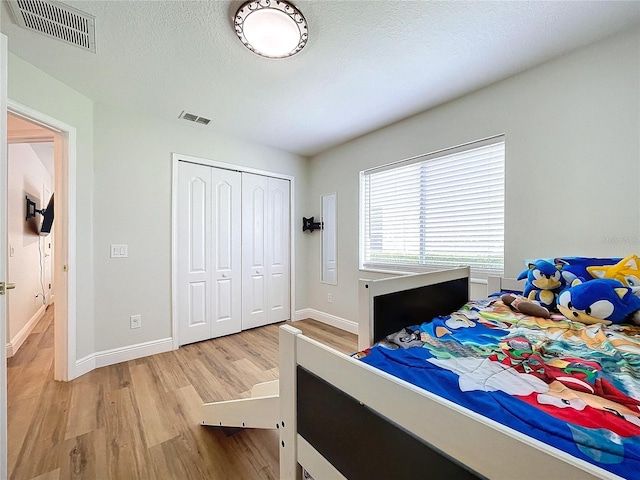 bedroom with a closet, a textured ceiling, visible vents, and wood finished floors