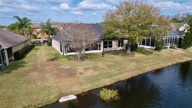 rear view of house with a yard, a water view, and a lanai