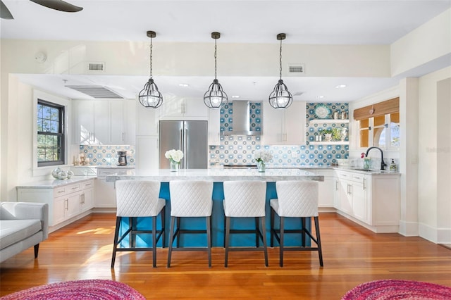 kitchen with white cabinetry, a kitchen island, high quality fridge, and wall chimney range hood