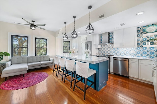 kitchen with white cabinetry, stainless steel appliances, a center island, and wall chimney exhaust hood