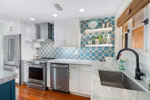 kitchen with sink, white cabinetry, stainless steel appliances, light stone counters, and wall chimney exhaust hood