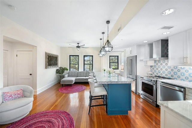 kitchen featuring high quality appliances, white cabinetry, a center island, and wall chimney range hood