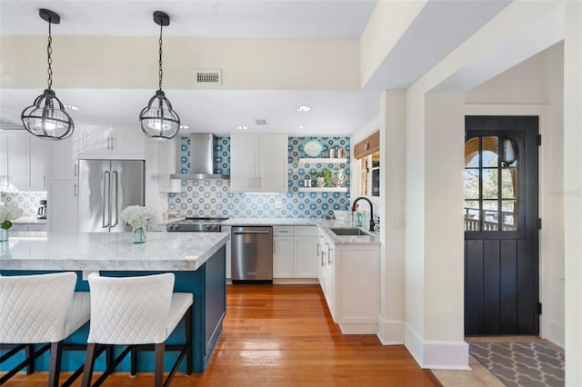 kitchen featuring pendant lighting, sink, appliances with stainless steel finishes, white cabinetry, and wall chimney exhaust hood