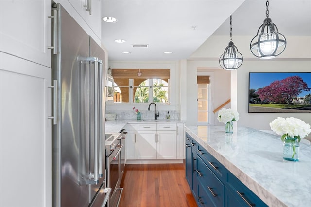 kitchen with blue cabinets, sink, high end refrigerator, pendant lighting, and light stone countertops