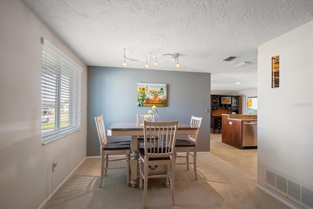 dining room featuring light colored carpet, track lighting, and a textured ceiling