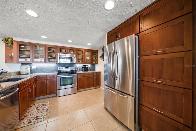 kitchen featuring light tile patterned flooring, tasteful backsplash, sink, stainless steel appliances, and light stone countertops