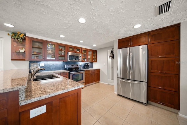 kitchen featuring sink, light tile patterned floors, appliances with stainless steel finishes, light stone counters, and decorative backsplash