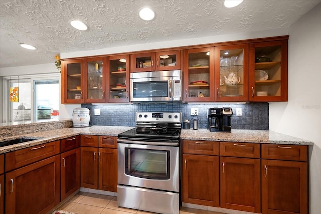 kitchen with light stone counters, a textured ceiling, light tile patterned floors, appliances with stainless steel finishes, and backsplash