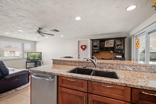 kitchen with sink, a textured ceiling, light tile patterned floors, dishwasher, and light stone countertops