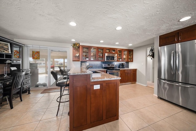 kitchen featuring light tile patterned flooring, appliances with stainless steel finishes, a kitchen breakfast bar, and light stone countertops