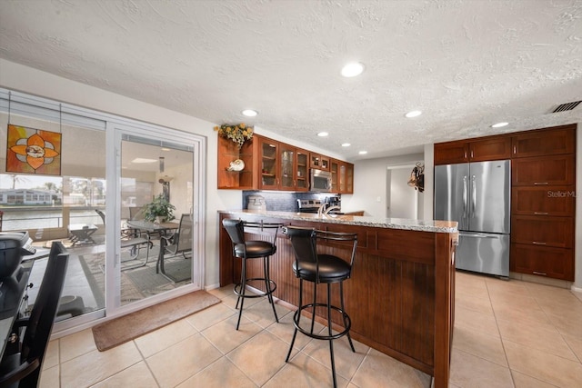 kitchen with appliances with stainless steel finishes, sink, light tile patterned floors, kitchen peninsula, and a textured ceiling