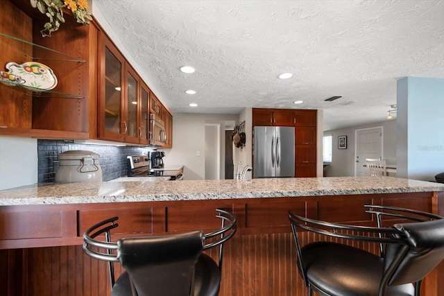 kitchen with a breakfast bar, appliances with stainless steel finishes, kitchen peninsula, and decorative backsplash