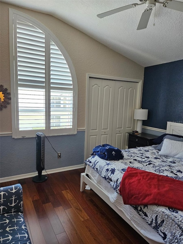 bedroom with lofted ceiling, a textured ceiling, dark hardwood / wood-style floors, a closet, and ceiling fan