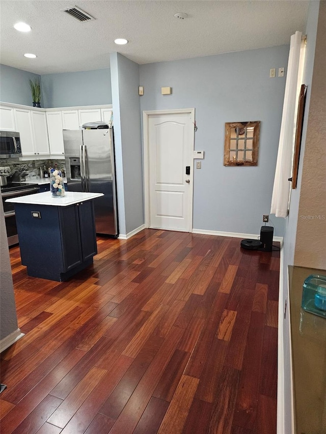 kitchen featuring white cabinetry, appliances with stainless steel finishes, dark hardwood / wood-style floors, a kitchen island, and backsplash