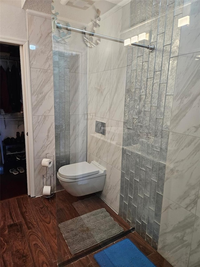 bathroom with a tile shower, hardwood / wood-style floors, toilet, and tile walls