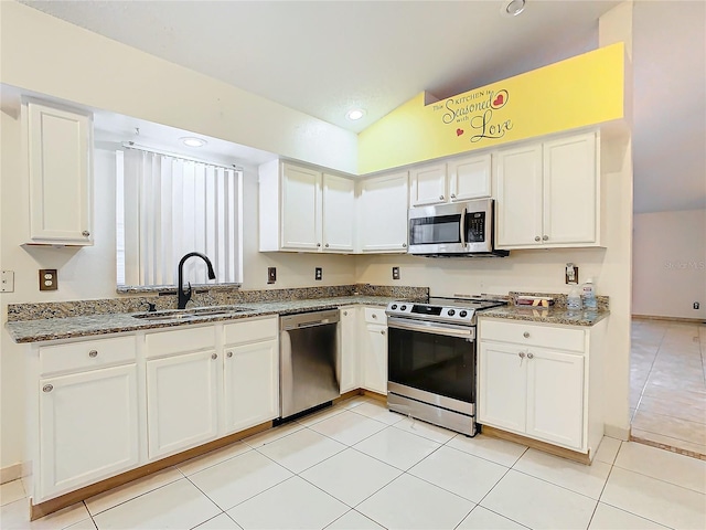 kitchen with sink, white cabinetry, vaulted ceiling, appliances with stainless steel finishes, and dark stone counters