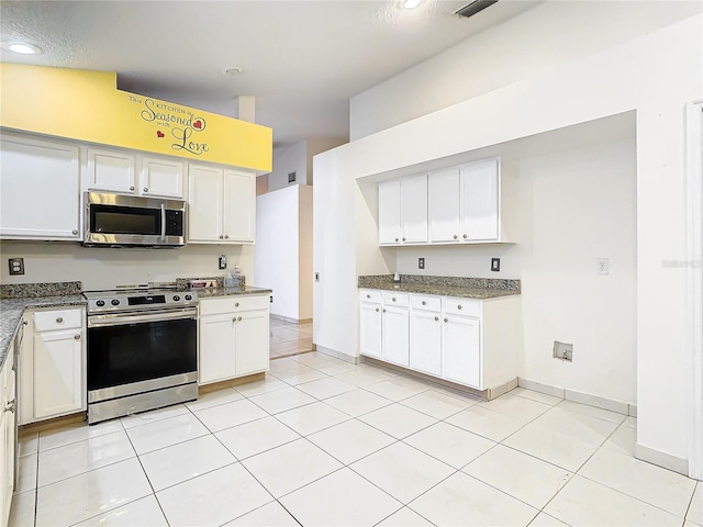 kitchen featuring white cabinetry, appliances with stainless steel finishes, light tile patterned floors, and dark stone countertops