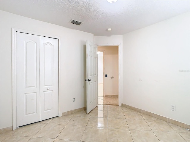 unfurnished bedroom with a closet, a textured ceiling, and light tile patterned floors