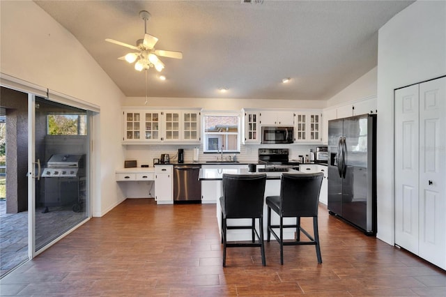 kitchen with a breakfast bar, white cabinetry, vaulted ceiling, a kitchen island, and stainless steel appliances