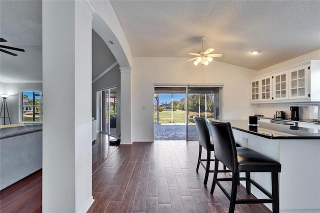 dining room featuring vaulted ceiling, dark hardwood / wood-style floors, decorative columns, ceiling fan, and a textured ceiling