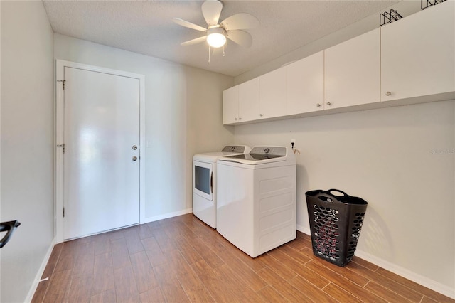 clothes washing area with cabinets, washing machine and dryer, a textured ceiling, and light wood-type flooring